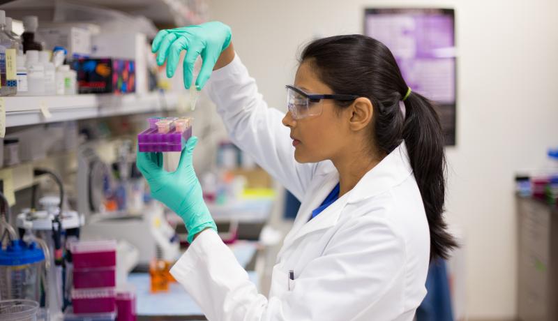 A close-up photo of a female scientist conducting an experiment in a lab.